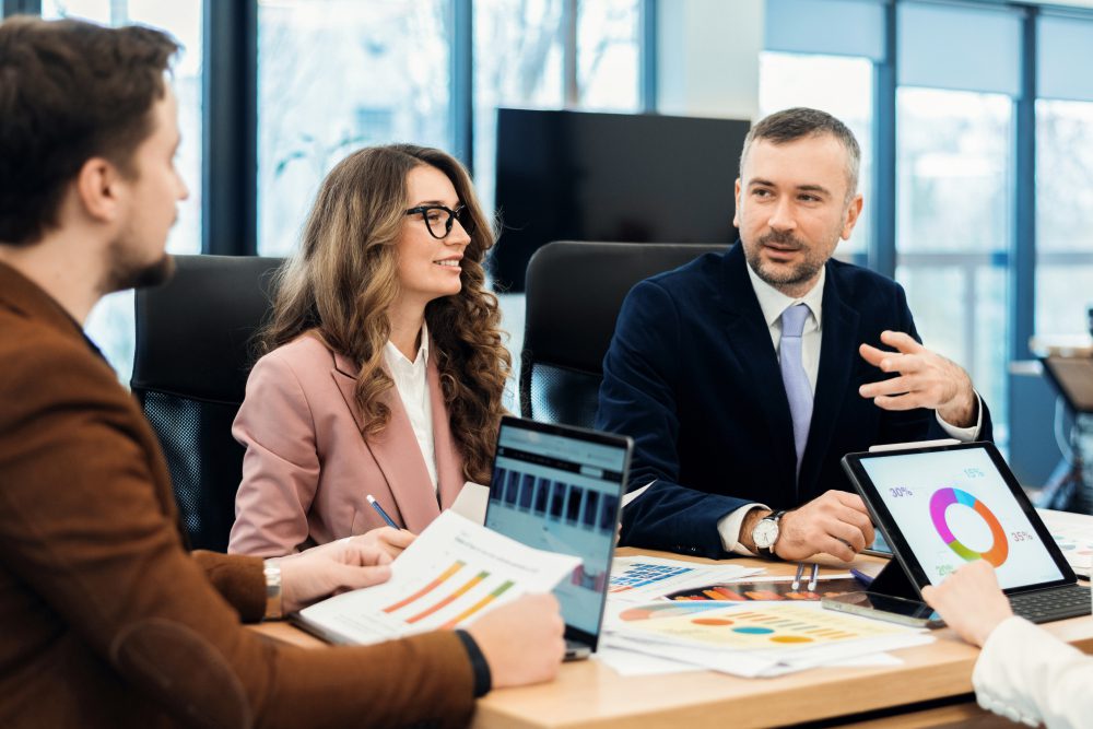 Three business people in an office meeting, looking at a laptop.