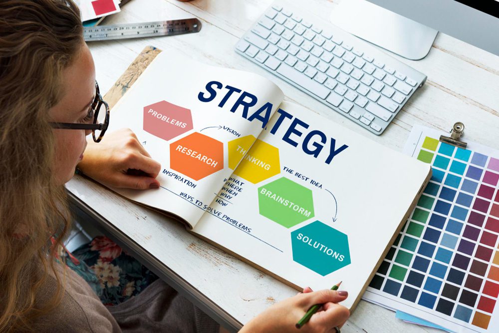 Hands working on a desk with a "STRATEGY" chart showing hexagonal steps.